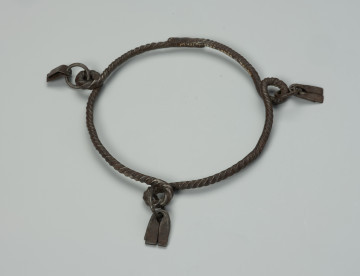 bransoleta, biżuteria - Ujęcie z góry. Zamknięta, żelazna, okrągła bransoleta z trzema pętelkami do których przymocowane są żelazne wisiorki w kształcie trapezu.