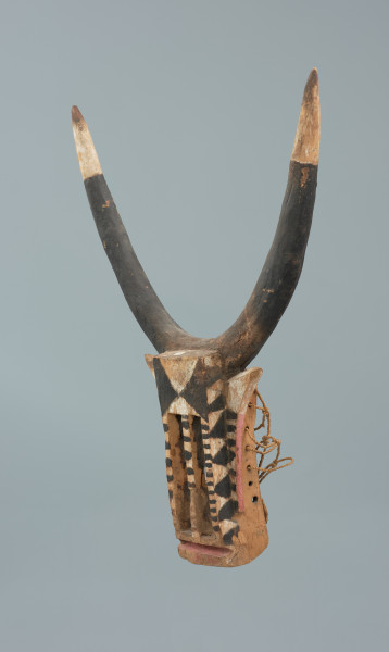 rzeźbiona maska - Ujęcie z przodu, z lewej strony. Drewniana, rzeźbiona maska byka, do której przymocowany jest bawełniany sznurek.