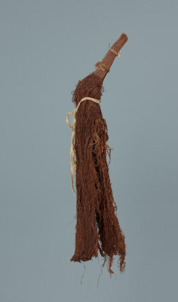 maska - Ujęcie z lewego boku. Maska wykonana z łyka drzewa, do której przymocowany jest bawełniany sznurek.