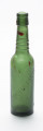 szklana butelka z trzema wypukłymi pierścieniami na szyjce - Ujęcie z przodu; Szklana butelka piwówka z grubego szkła butelkowego w ciemnym kolorze oliwkowo-zielonym. Szyjka wyodrębniona trzema wypukłymi pierścieniami liniowymi umieszczonymi w dolnej części szyjki. W górnej partii szyjki, poniżej wylewu zgrubienie z otworami na zamknięcie pałąkowe (brak). Ślady szwów bocznych pionowych. Dno nieco zagłębione.