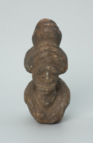 rzeźba; popiersie; Figura kultu zmarłych - Ujęcie z przodu. Rzeźbione w grafitowobeżowym steatycie popiersie człowieka z jaszczurką, której łapy obejmują głowę i ramiona postaci ludzkiej.