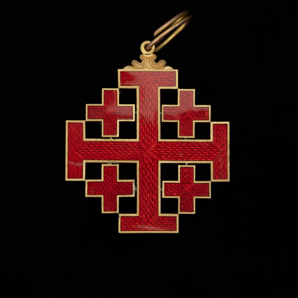 Order Grobu Świętego - Ujęcie rewersu. Krzyż laskowany w kątach którego cztery krzyże greckie. Ramiona krzyży pokryte czerwoną emalią ze złotą obwódkach po brzegach. U góry motyw floralny w którym uszko z podłużną zawieszką.