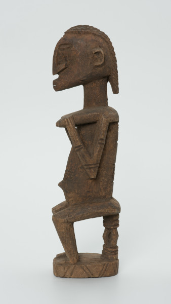 drewniana, rzeźbiona figura - Ujęcie z prawego boku. Drewniana, rzeźbiona figura kobiety siedzącej na stołku.