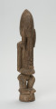 drewniana, rzeźbiona figura - Ujęcie z przodu, z prawej strony. Drewniana, rzeźbiona postać ludzka. Twarz schematycznie zaznaczona, zakończona bardzo długą brodą/podbródkiem. Po obu stronach brody dwa długie wąsy.