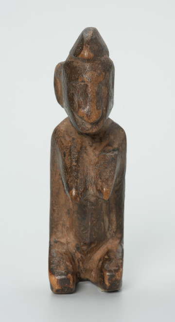 drewniana figura - Ujęcie z przodu. Drewniana, rzeźbiona figura. Twarz ledwie zaznaczona, tułów prosty, dobrze zaznaczone piersi, stopy zaznaczone symbolicznie.