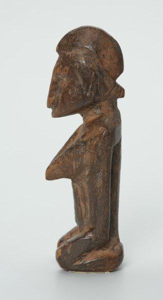 drewniana figura - Ujęcie lewego boku. Drewniana, rzeźbiona figura. Twarz ledwie zaznaczona, tułów prosty, dobrze zaznaczone piersi, stopy zaznaczone symbolicznie.