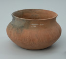 Naczynie gliniane (waza) - Ujęcie z tyłu. Naczynie gliniane (waza) o przysadzistych proporcjach, barwy jasnobrunatnej. Brzusiec wazy jest w całości zdobiony dookolnie nieregularnymi skośnymi płytkimi bruzdami.