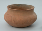 Naczynie gliniane (waza) - Ujęcie z przodu. Naczynie gliniane (waza) o przysadzistych proporcjach, barwy jasnobrunatnej. Brzusiec wazy jest w całości zdobiony dookolnie nieregularnymi skośnymi płytkimi bruzdami.