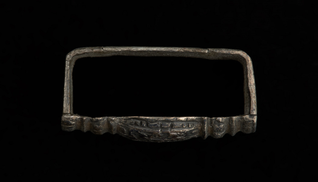 Szlufka do pendentu księcia Kazimierza VI/IX (1557-1605) - Ujęcie z boku z dołu. Prostokątna szlufka wykonana z gładkiej, srebrnej taśmy, z ozdobnie opracowaną częścią przednią w formie tralki, pokrytą grawerowaną i niellowaną dekoracją.