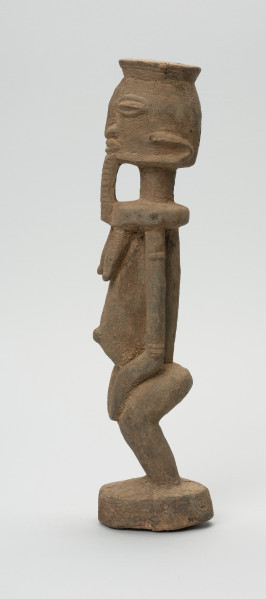 rzeźbiona figura - Ujęcie lewego boku. Drewniana, rzeźbiona postać, z zaznaczonymi jednocześnie cechami płciowymi męskimi i żeńskimi. Wyodrębnione cechy męskie to broda, żeńskie: piersi.