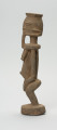 rzeźbiona figura - Ujęcie lewego boku. Drewniana, rzeźbiona postać, z zaznaczonymi jednocześnie cechami płciowymi męskimi i żeńskimi. Wyodrębnione cechy męskie to broda, żeńskie: piersi.