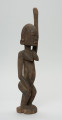 rzeźbiona figura - Ujęcie z przodu, z prawej strony. Drewniana, rzeźbiona postać kobiety. Jej lewa ręka podniesiona jest do góry.