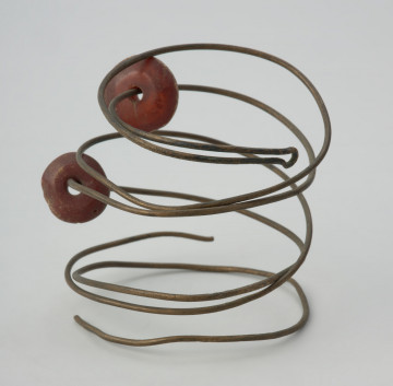 Spirala z brązowego drutu - Ujęcie spirali w pionie. Trzyzwojowa spirala z cienkiego brązowego drutu, na który nawleczone są dwa bursztynowe paciorki.