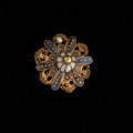 pontalik z sarkofagu księcia Franciszka I (1577-1620) - Ujęcie z przodu na czarnym tle. Pontalik w kształcie kwiatowej rozetki z płatkami zdobionymi perełkami nawleczonymi na drut oraz emalią komórkową, inkrustowaną złotem. Płatki z perełkami otoczone są skręconym drutem. Środek kwiatka kopulasty, zbudowany z ośmiu białych płatków, zwieńczony złotą kulką. Na odwrocie centralnie przymocowane uszko z drutu.