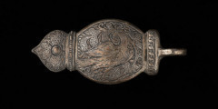 Zapinka pendentu (3części), księcia Kazimierza VI/IX (1557-1605) - Ujęcie w powiększeniu zapięcia. Sprzączka pasa składająca się z trzech elementów. Dwa skrajne o migdałowym kształcie, z jednej strony zakończone profilowanym przewężeniem i łukiem w ośli grzbiet, z drugiej mają przylutowane poprzecznie koliste uszka z gładkiego drutu. Środkowy element sprzączki,zdobiony jest guzem ujętym od góry i dołu profilowanymi sterczynami; po prawej stronie uszko, którym połączony jest z bocznym elementem zapinki, a po lewej - esowato wygięty haczyk, służący do zapinania pasa. Wszystkie części zapinki pokryte są gęsto grawerowaną, niellowaną dekoracją z motywami ptaków wśród wici roślinnej oraz stylizowanych kwiatów i ornamentem geometrycznym.