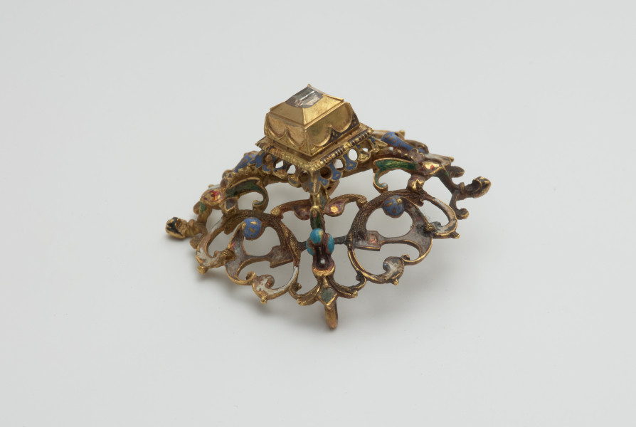 biżuteria, ozdoby - Ujęcie z boku z góry. Ażurowy klejnot z kołpaka z diamentem, zdobiony barwną emalią.