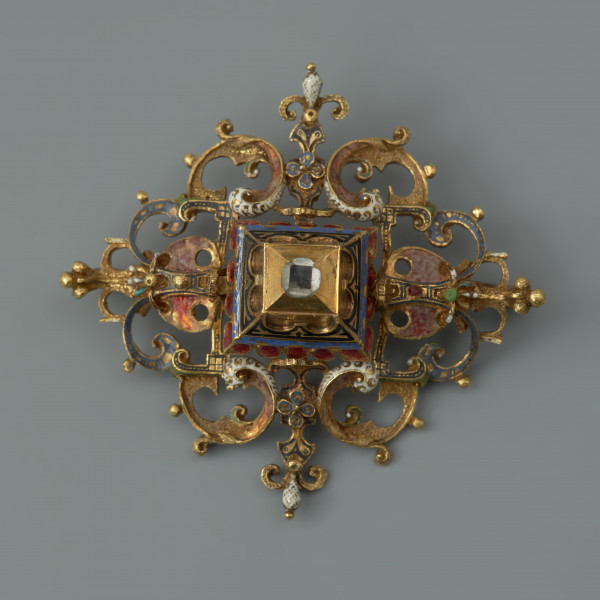 rozeta z kołpaka księcia Filipa II (1573-1618) - Ujęcie z przodu. Klejnot zbudowany z dwóch skręconych śrubą części: ażurowego stelaża o romboidalnym kształcie i osadzonej na nim wysokiej, kasetowej oprawy, ujmującej diament o szlifie tablicowym. Stelaż i ścianki kasztu pokryte są barwną emalią, korpusową, a także żłobkową, z wzorami rezerwowanymi w złocie. Rozety mają na spodniej stronie, w narożach, haczyki umożliwiające spinanie ich w łańcuch, a także uszka pozwalające na ich mocowanie do stroju.
