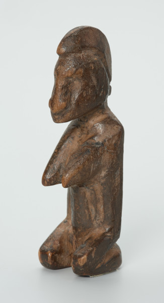 drewniana figura - Ujęcie z przodu skosem w lewą stronę. Drewniana, rzeźbiona figura. Twarz ledwie zaznaczona, tułów prosty, dobrze zaznaczone piersi, stopy zaznaczone symbolicznie.