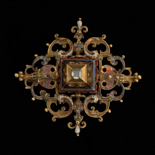 rozeta z kołpaka księcia Filipa II (1573-1618) - Ujęcie z przodu na czarnym tle. Klejnot zbudowany z dwóch skręconych śrubą części: ażurowego stelaża o romboidalnym kształcie i osadzonej na nim wysokiej, kasetowej oprawy, ujmującej diament o szlifie tablicowym. Stelaż i ścianki kasztu pokryte są barwną emalią, korpusową, a także żłobkową, z wzorami rezerwowanymi w złocie. Rozety mają na spodniej stronie, w narożach, haczyki umożliwiające spinanie ich w łańcuch, a także uszka pozwalające na ich mocowanie do stroju.