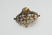 biżuteria, ozdoby - Ujęcie z boku z dołu. Ażurowy klejnot z kołpaka z diamentem, zdobiony barwną emalią.