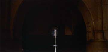 fotografia - Ujęcie z przodu. Fotografia barwna pod pleksi na dibondzie z przedstawieniem wnętrza kruchty kościoła z pionową smugą światła w centrum kompozycji i głową białego kota u podstawy filaru po lewej.