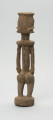 rzeźbiona figura - Ujęcie z tyłu. Drewniana, rzeźbiona postać, z zaznaczonymi jednocześnie cechami płciowymi męskimi i żeńskimi. Wyodrębnione cechy męskie to broda, żeńskie: piersi.