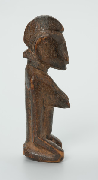 drewniana figura - Ujęcie lewego boku. Drewniana, rzeźbiona figura. Twarz ledwie zaznaczona, tułów prosty, dobrze zaznaczone piersi, stopy zaznaczone symbolicznie.