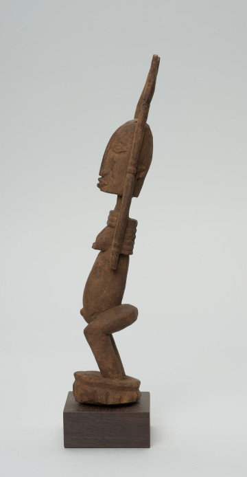 rzeźba - Ujęcie lewego boku. Figura przedstawiajaąca postać kobiety z rękoma uniesionymi do góry. Ręce są nie proporcjonalnie długie.