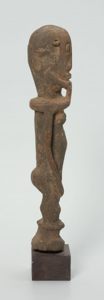 Drewniana figurka androgyniczna - Ujęcie z prawej strony; drewniana figurka przedstawiająca postać z brodą i piersiami. Statyczna, zgeometryzowana. Ręce wyodrębnione z tułowia.