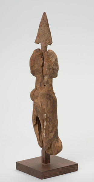 rzeźba - Ujęcie tyłu i prawej strony rzeźby. Uproszczona postać ludzka, z wetkniętym grotem strzały. Na wysokości nogi widnieje numer inwentarzowy. Rzeźba stanowi część wyposażenia grobu.