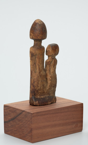 rzeźba - Ujęcie z przodu z prawej strony. Drewniane, rzeźbione dwie postaci ludzkie, różnej wysokości umieszczone na jednej podstawie. Bardzo schematyczne, z walcowatego tułowia wyodrębniona jedynie głowa na długiej szyi.