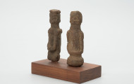 rzeźba - Ujęcie ze skosu z prawej; Zestaw składa się z dwóch małych, drewnianych figurek przedstawiających postacie ludzkie w pozycji stojącej. Rzeźby o uproszczonej formie i masywnej budowie ciała.