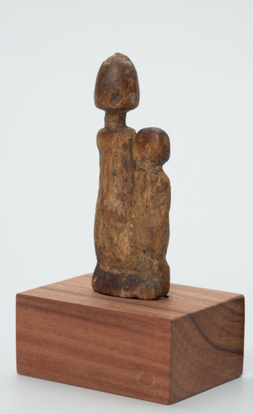 rzeźba - Ujęcie z przodu z lewej strony. Drewniane, rzeźbione dwie postaci ludzkie, różnej wysokości umieszczone na jednej podstawie. Bardzo schematyczne, z walcowatego tułowia wyodrębniona jedynie głowa na długiej szyi.