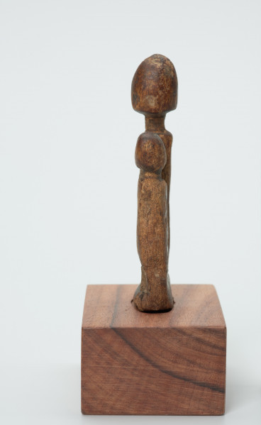 rzeźba - Ujęcie lewego boku. Drewniane, rzeźbione dwie postaci ludzkie, różnej wysokości umieszczone na jednej podstawie. Bardzo schematyczne, z walcowatego tułowia wyodrębniona jedynie głowa na długiej szyi.