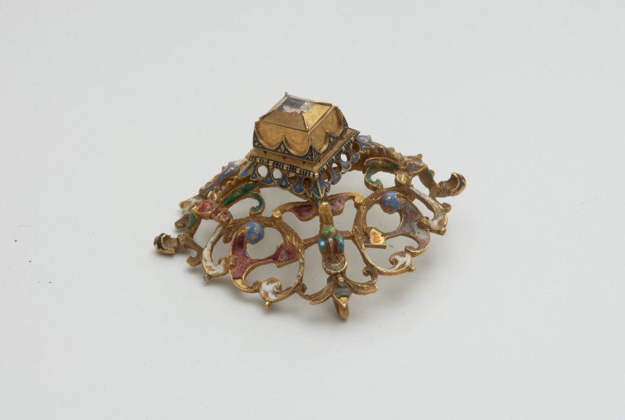 biżuteria, ozdoby - Ujęcie z boku z góry. Ażurowy klejnot z kołpaka z diamentem, zdobiony barwną emalią.