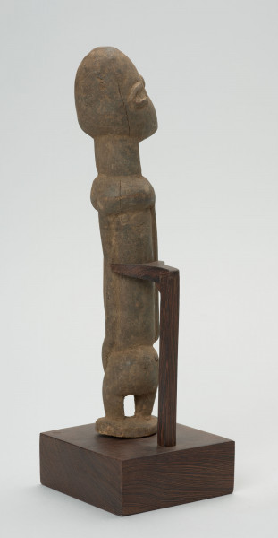 rzeźba - Ujęcie ze skosu z tyłu; Figura - postać przodka. Głowa i korpus w stosunku do nóg bardzo duże - co typowe jest dla sztuki dogońskiej. Ręce bardzo długie sięgające kolan. Figura wsparta na konstrukcji przymocowanej do podstawy.