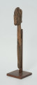 Ujęcie ze skosu z prawej; Rzeźba. Figura - Nommo - drewniana pałka zakończona głową o cechach antropomorficznych. Na głowie widoczne spękania.