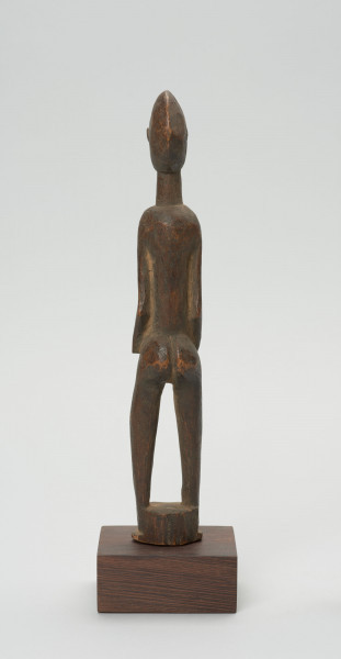 rzeźba - Ujęcie z tyłu; Figura - postać kobiety w pozycji stojącej. Głowa mała, podłużna, ręce, piersi, brzuch lekko wydobyte z bryły figury. Nogi bez stóp, przechodzą od razu w okrągły cokolik.