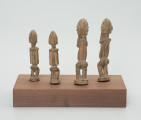 rzeźba - Ujęcie z tyłu na wprost; Zestaw składa się z czterech jasnych, drewnianych figurek przedstawiających postacie ludzkie w pozycji stojące – jedna para mniejsza, a druga większa. Większa para ma zakryte dłońmi oczy.