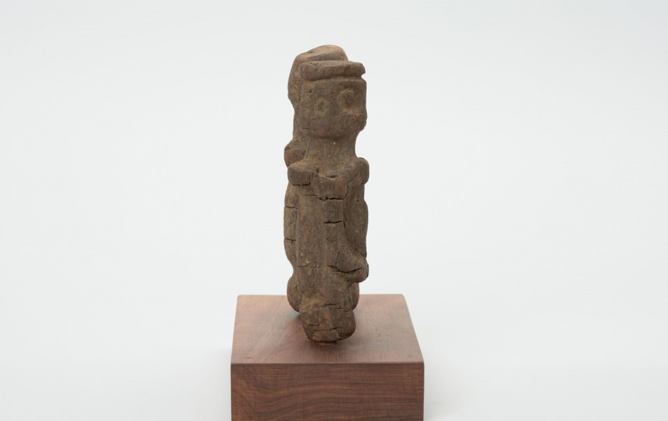 rzeźba - Ujęcie z boku; Zestaw składa się z dwóch małych, drewnianych figurek przedstawiających postacie ludzkie w pozycji stojącej. Rzeźby o uproszczonej formie i masywnej budowie ciała. Nieregularne kształty oraz widoczne spękania.