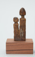rzeźba - Ujęcie z tyłu. Drewniane, rzeźbione dwie postaci ludzkie, różnej wysokości umieszczone na jednej podstawie. Bardzo schematyczne, z walcowatego tułowia wyodrębniona jedynie głowa na długiej szyi.
