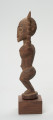 rzeźba - Ujęcie prawej strony. Figura mężczyzny w pozycji stojącej (na ugiętych w kolanach nogach) z rękoma uniesionymi do góry. Cała powierzchnia rzeźby pokryta jest delikatnym rytem, sugerującym skaryfikację.