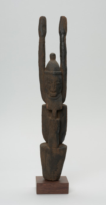 rzeźba - Ujęcie z przodu. Figurka przedstawia Hogona – kapłana kultu Lebe. Widoczna broda, wyprostowane ręce uniesione do góry.
