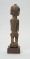 rzeźba - Ujęcie z tyłu. Figura przedstawiająca mężczyznę stojącego na nogach ugiętych w kolanach. Głowa duża, zaokrąglona, oczy duże, ze źrenicami, wyraźnie zaznaczona bródka.