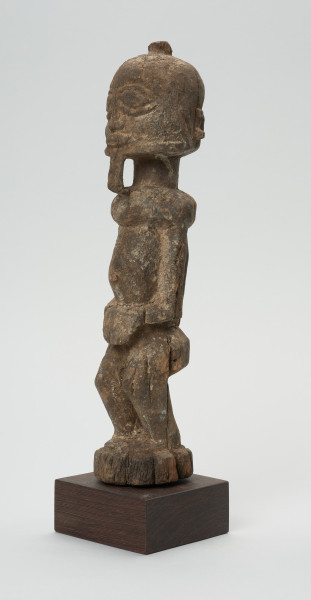rzeźba - Ujęcie z przodu z lewej strony. Figura przedstawiająca mężczyznę stojącego na nogach ugiętych w kolanach. Głowa duża, zaokrąglona, oczy duże, ze źrenicami, wyraźnie zaznaczona bródka.