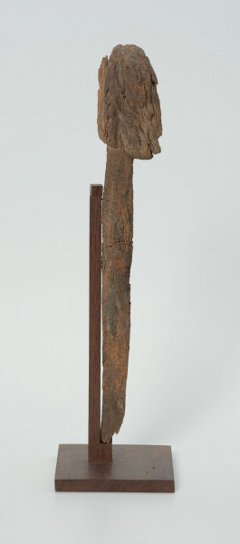 Ujęcie z lewego boku. Rzeźba. Figura - Nommo - drewniana pałka zakończona głową o cechach antropomorficznych. Widoczne spękania na calej głowie.