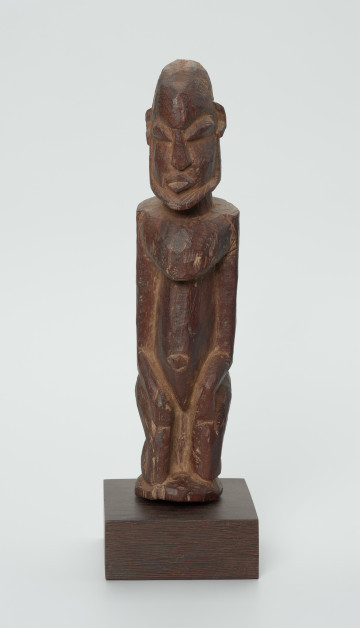 Drewniana figurka mężczyzny z brodą - Ujęcie z przodu. Drewniana figurka mężczyzny siedzącego na stołku. Kompozycja zgeometryzowana. Na twarzy zaznaczona broda. Głowa bez włosów.