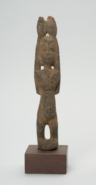 rzeźba - Ujęcie z przodu. Drewniana rzeźba postaci kobiety. Długie ręce wzniesione do góry, głowa podłużna, wyraźnie zaznaczone duże oczy, zarysowany wypukły brzuch, krótkie, lekko skrzywione nogi.