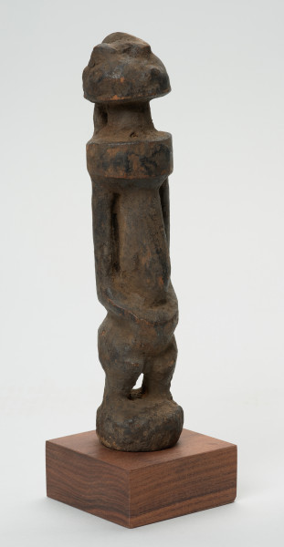 rzeźba - Ujęcie przodu skosem w prawą stronę. Rzeźba w drewnie w formie uproszczonej. Przedstawia postać męską o lekko zarysowanej głowie, szczupłym, długim tułowiu, krótkie nogi ugięte, ręce oparte na kolanach.