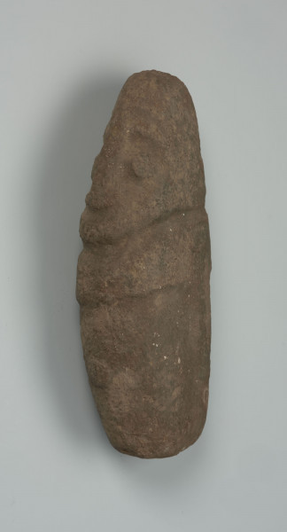 Kamienna figura antropomorficzna - Ujęcie z prawej strony; obiekt leżący; kamienna figura owalna, podłużna, rzeźbiona płytkimi uderzeniami, z zaznaczonymi oczami i wąskim nosem.
